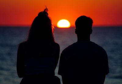 A silhouette of a couple enjoying the beautiful sunset on the shore of the sea