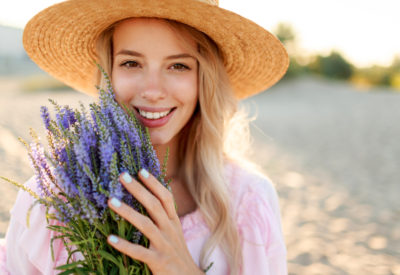 Smiling pretty woman  in  straw hat posing on sunny beach near ocean with bouquet of flowers. Close up portrait.