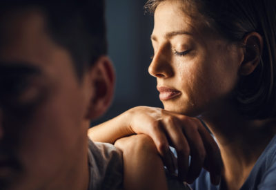 Sad woman crying with eyes closed while leaning on boyfriend's shoulder.