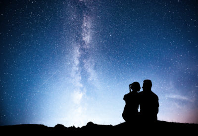 Milky Way with silhouette of people. Landscape with night starry sky. Standing man and woman on the mountain with star light. Hugging couple against purple milky way. Beautiful galaxy. Universe.