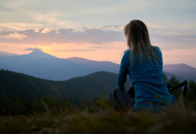 Back view of woman hiker resting after day of hike and watching at sunrise above mountain beskids. Tourist enjoying landscape of mountain hills and morning sky. Concept of travelling, hiking.