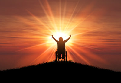 3D render of a silhouette of a female in a wheelchair with her arms raised against a sunset ocean