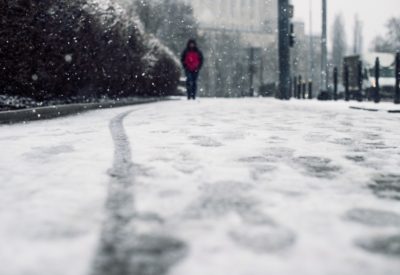 A low angle shot of a person walking on the snow covered sidewalk under the snow