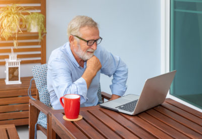 Senior man executive with white hair using computer laptop watching movie at home with coffee