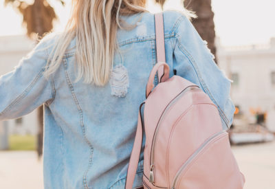 pretty woman walking in city street in stylish denim oversize jacket, holding pink leather backpack, summer style trend
